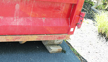 Dumpster set on wooden blocks to protect a driveway